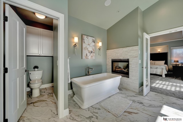 bathroom featuring lofted ceiling, a stone fireplace, a tub, and toilet