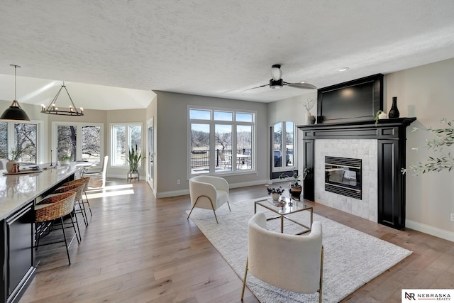 living room with a tiled fireplace, ceiling fan with notable chandelier, a textured ceiling, and light hardwood / wood-style flooring