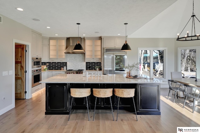 kitchen with a spacious island, wall chimney exhaust hood, stainless steel appliances, and hanging light fixtures