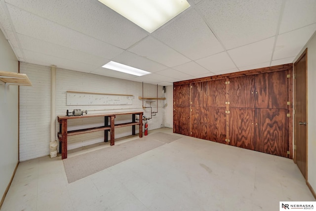 basement with a paneled ceiling, a workshop area, and brick wall