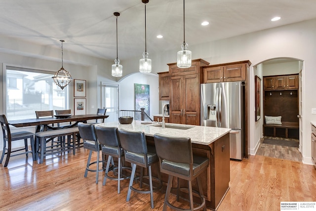 kitchen with pendant lighting, stainless steel fridge, an island with sink, and light stone counters