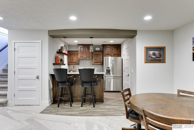 kitchen featuring pendant lighting, stainless steel fridge, a breakfast bar area, light carpet, and decorative backsplash