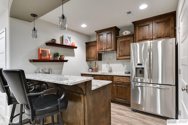 kitchen featuring pendant lighting, sink, a breakfast bar area, stainless steel fridge with ice dispenser, and light stone countertops