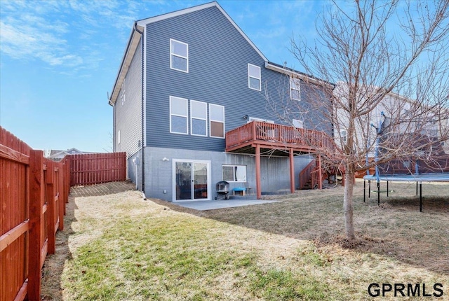 back of house with a wooden deck, a yard, a patio, and a trampoline