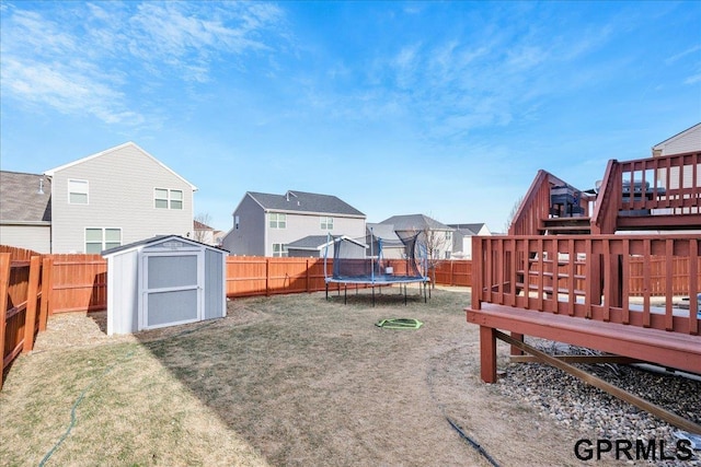 view of yard with a wooden deck, a trampoline, and a storage shed