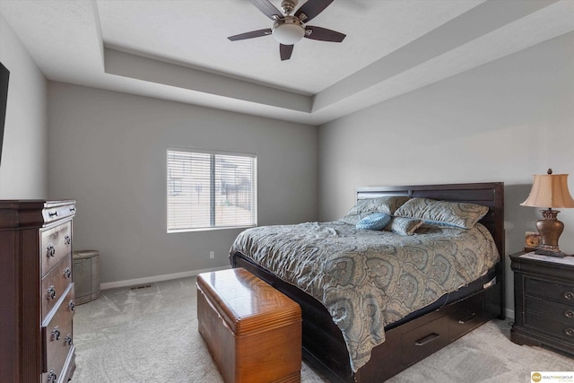 carpeted bedroom with ceiling fan and a raised ceiling