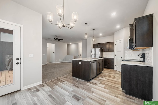 kitchen featuring appliances with stainless steel finishes, backsplash, dark brown cabinets, a center island with sink, and decorative light fixtures