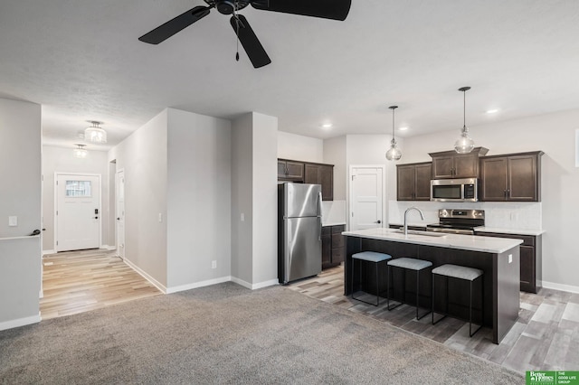 kitchen with sink, appliances with stainless steel finishes, dark brown cabinets, a center island with sink, and decorative light fixtures