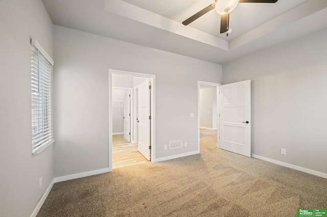 unfurnished bedroom featuring a tray ceiling, ensuite bath, and light colored carpet