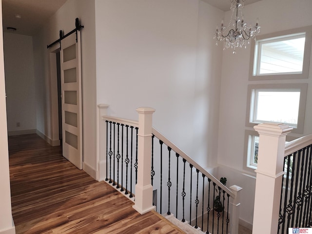 staircase featuring an inviting chandelier, hardwood / wood-style flooring, a barn door, and a towering ceiling