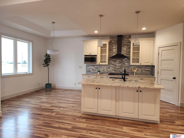 kitchen featuring wall chimney exhaust hood, sink, tasteful backsplash, a center island with sink, and pendant lighting