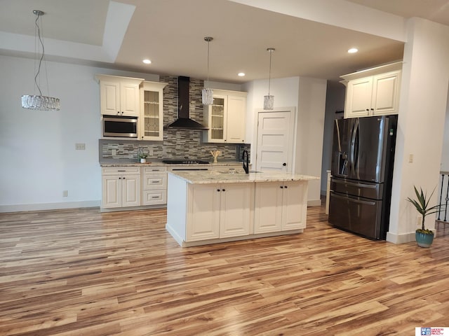 kitchen featuring white cabinetry, black appliances, a center island with sink, and wall chimney range hood