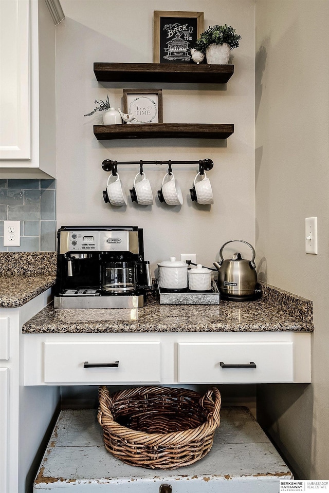 bar with tasteful backsplash, white cabinetry, and dark stone countertops