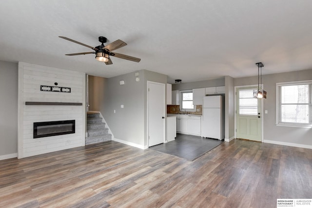 unfurnished living room featuring dark wood-type flooring, a large fireplace, ceiling fan, and sink