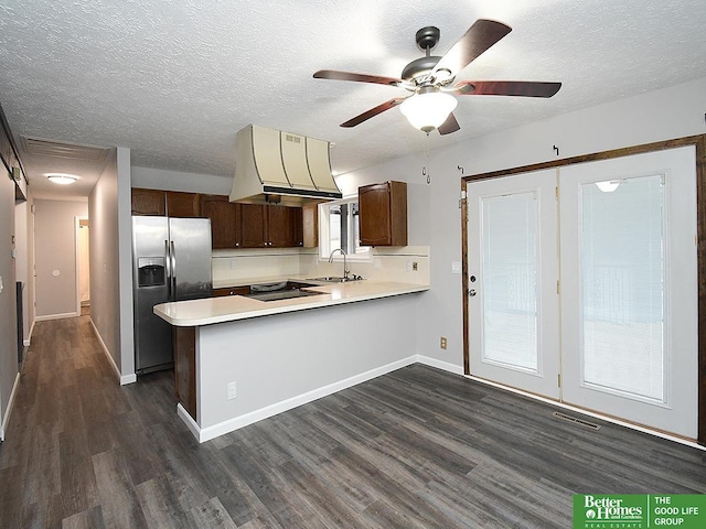 kitchen featuring island range hood, stainless steel fridge with ice dispenser, dark brown cabinets, dark hardwood / wood-style floors, and kitchen peninsula