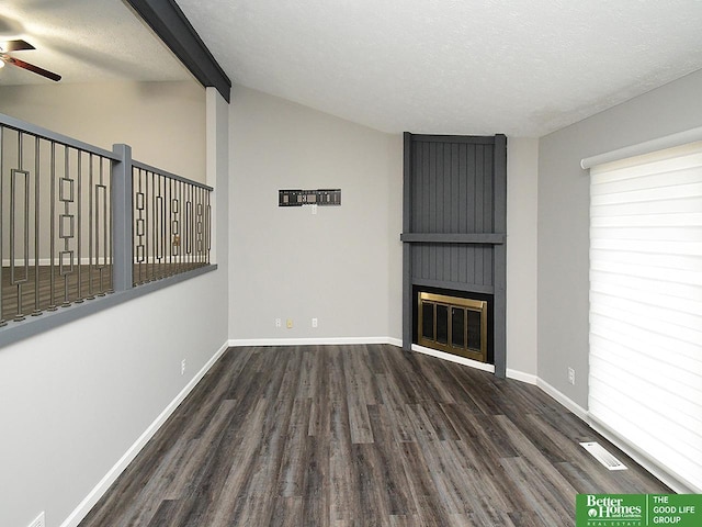 unfurnished living room with dark hardwood / wood-style floors, lofted ceiling with beams, a large fireplace, ceiling fan, and a textured ceiling