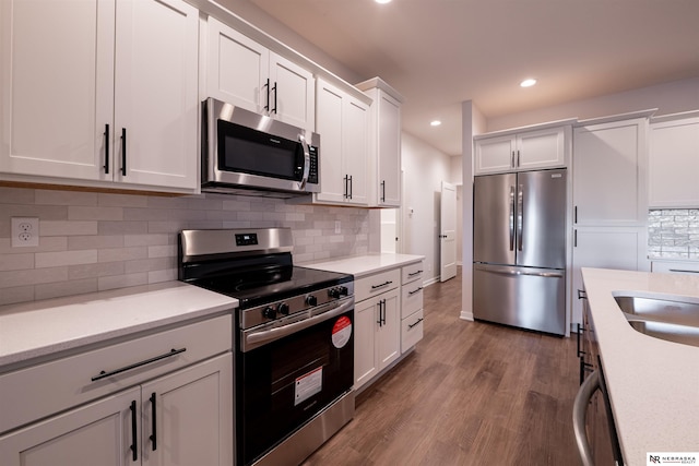 kitchen with sink, wood-type flooring, white cabinets, stainless steel appliances, and backsplash