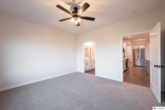 unfurnished bedroom featuring dark carpet, stainless steel fridge, ceiling fan, and ensuite bathroom