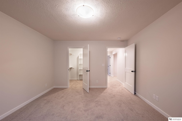 unfurnished bedroom featuring a spacious closet, light carpet, a textured ceiling, and a closet