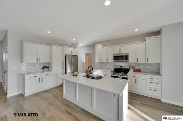 kitchen with a kitchen island with sink, stainless steel appliances, a sink, white cabinetry, and light wood-type flooring