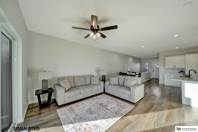 living room featuring baseboards, ceiling fan, light wood-style flooring, and recessed lighting