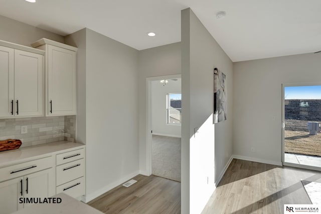 kitchen with visible vents, white cabinets, light countertops, light wood-type flooring, and backsplash