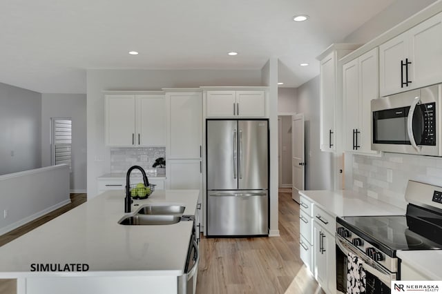 kitchen featuring a kitchen island with sink, a sink, white cabinets, light wood-style floors, and appliances with stainless steel finishes