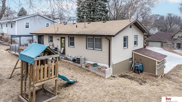 rear view of house with central AC unit, an outbuilding, a garage, and a playground