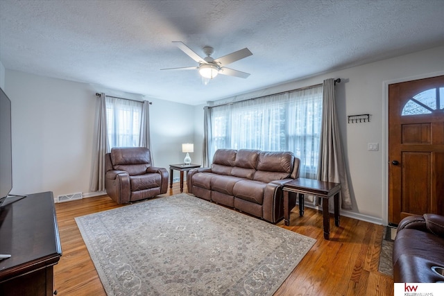 living room with ceiling fan, a textured ceiling, and light hardwood / wood-style floors