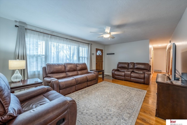 living room with ceiling fan, a textured ceiling, and light hardwood / wood-style floors