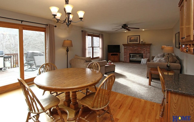 dining area with ceiling fan with notable chandelier, a brick fireplace, and light hardwood / wood-style flooring