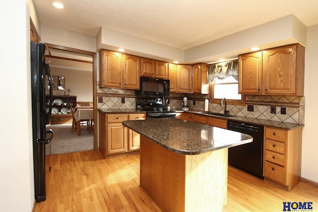 kitchen with sink, black appliances, a kitchen island, decorative backsplash, and light wood-type flooring