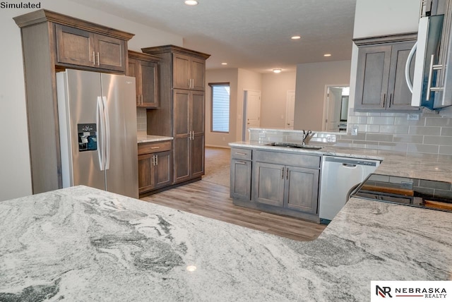 kitchen with sink, light stone counters, tasteful backsplash, light wood-type flooring, and stainless steel appliances