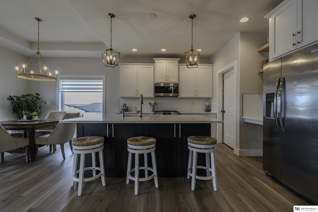 kitchen featuring white cabinetry, hanging light fixtures, an island with sink, and appliances with stainless steel finishes