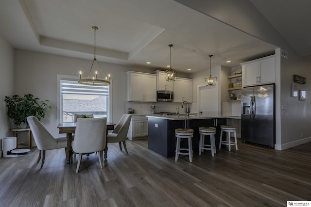 kitchen with stainless steel appliances, a kitchen island with sink, pendant lighting, and white cabinets