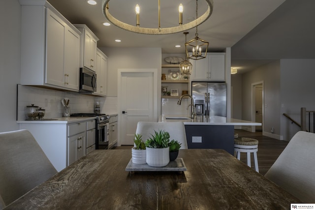 kitchen featuring decorative light fixtures, tasteful backsplash, white cabinetry, stainless steel appliances, and a center island with sink