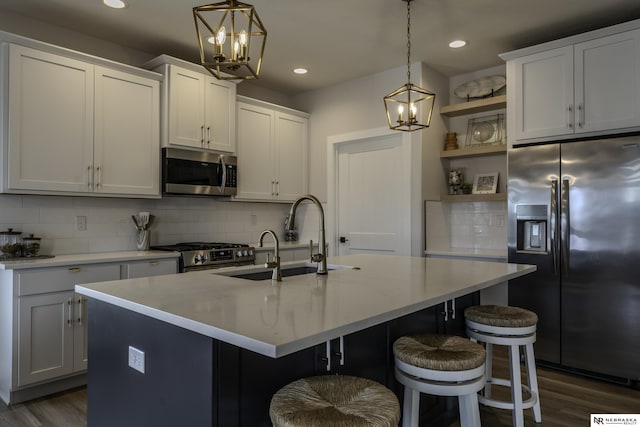 kitchen featuring pendant lighting, sink, stainless steel appliances, white cabinets, and a center island with sink