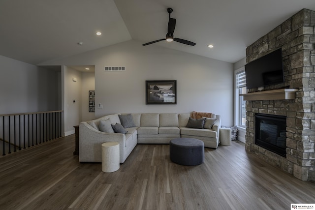 living room with ceiling fan, wood-type flooring, a stone fireplace, and vaulted ceiling