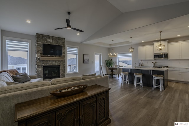 living room with sink, dark wood-type flooring, a fireplace, ceiling fan with notable chandelier, and vaulted ceiling