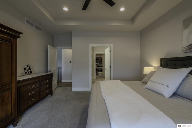 carpeted bedroom featuring ceiling fan, a tray ceiling, and a spacious closet