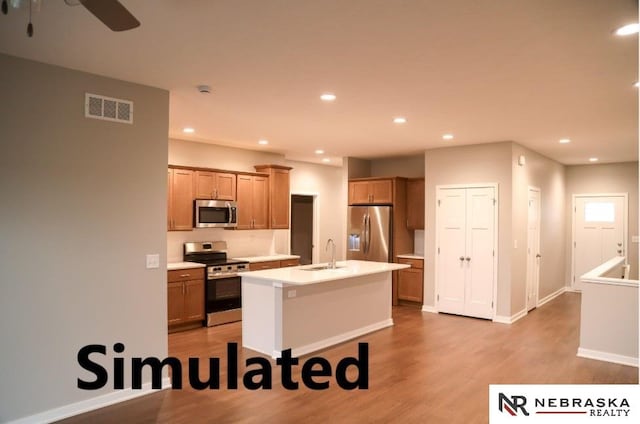 kitchen with appliances with stainless steel finishes, an island with sink, wood-type flooring, sink, and ceiling fan