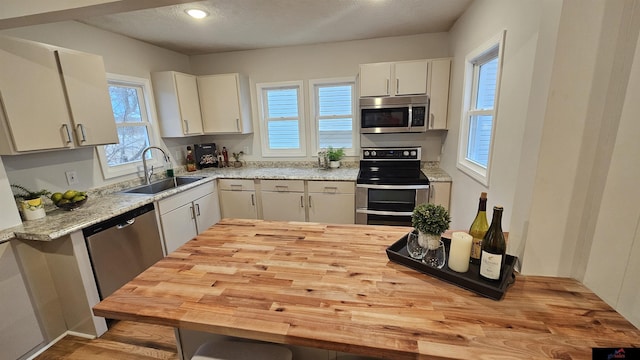 kitchen featuring stainless steel appliances, sink, white cabinets, and light stone counters