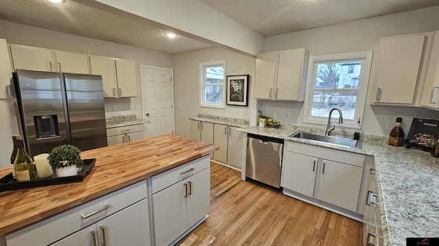 kitchen featuring sink, light hardwood / wood-style flooring, appliances with stainless steel finishes, white cabinets, and wood counters