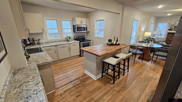 kitchen featuring a breakfast bar, sink, light stone counters, stainless steel appliances, and light hardwood / wood-style flooring