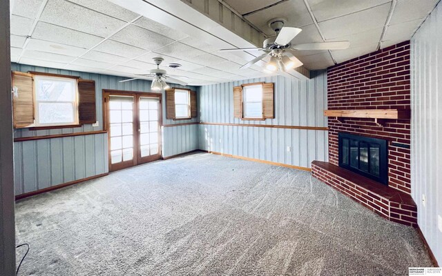 unfurnished living room featuring french doors, a paneled ceiling, carpet, and a brick fireplace