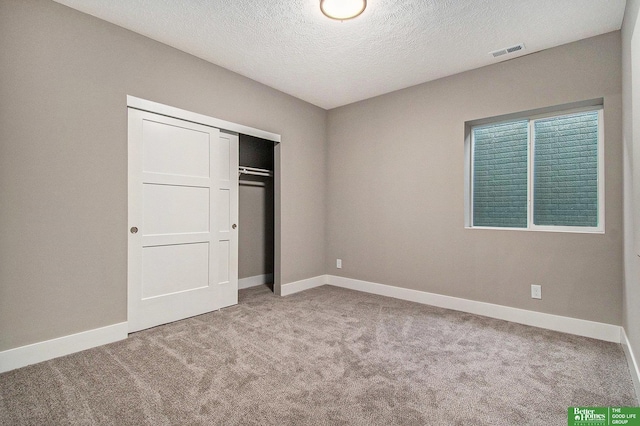 unfurnished bedroom featuring light carpet, a closet, and a textured ceiling