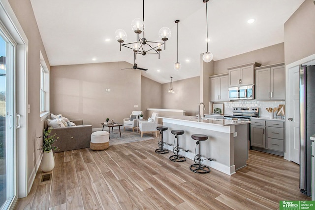 kitchen featuring gray cabinets, appliances with stainless steel finishes, a breakfast bar, pendant lighting, and an island with sink