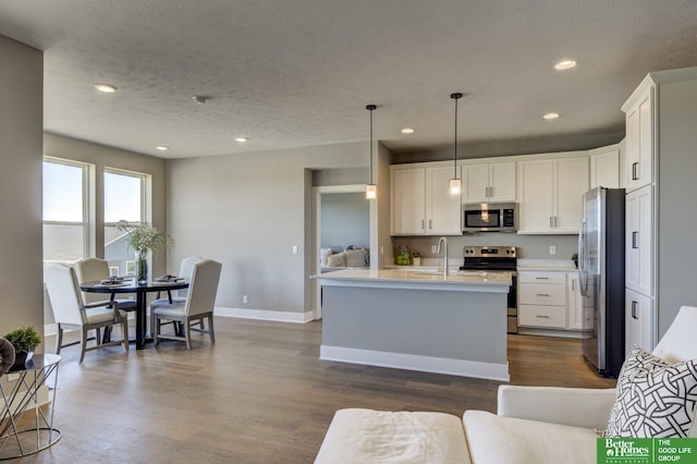 kitchen featuring stainless steel appliances, a center island with sink, white cabinets, and decorative light fixtures