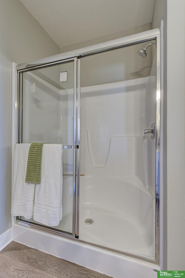 bathroom with hardwood / wood-style floors, a textured ceiling, and a shower with shower door