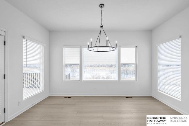 unfurnished dining area featuring an inviting chandelier and light hardwood / wood-style flooring